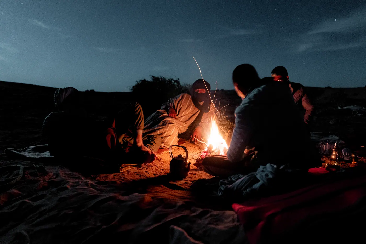 Menschen sitzen abends um ein Lagerfeuer